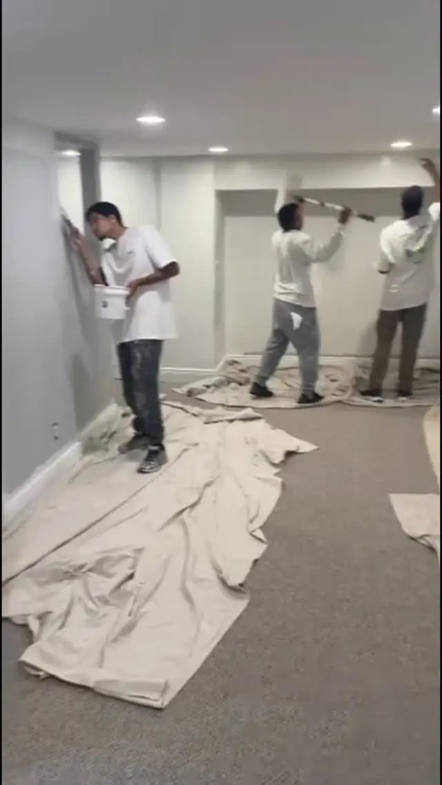 Three Paulo Painting crew members painting the walls of a room over drop cloths